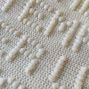 Könnte beinhalten: Nahaufnahme einer weißen Häkeldecke mit einem strukturierten Muster aus erhabenen Kreisen.