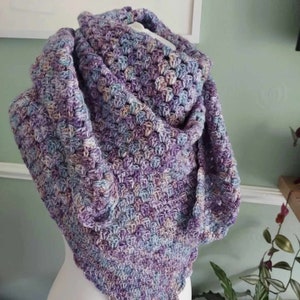May include: A crocheted shawl in shades of purple, blue, and white. The shawl is made with a textured stitch and has a triangular shape.