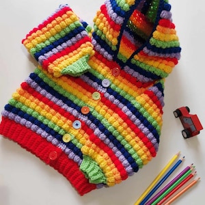 Può includere: Un cardigan con cappuccio a righe arcobaleno lavorato a uncinetto con chiusura a bottoni. Il cardigan è realizzato con una maglia testurizzata che crea una superficie irregolare.