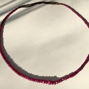 Può includere: Una lunga collana fatta di piccole perle di rubino sfaccettate. La collana è infilata su una catena d'argento.
