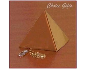 May include: A gold-toned metal pyramid with a 2.5 inch base edge, featuring the text Choice Gifts at the top. A small silver-toned charm with an Egyptian-style cartouche design and a delicate chain are positioned in front of the pyramid base.