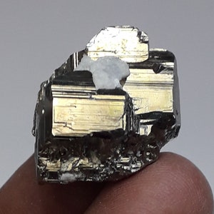 May include: A large, dark gray, metallic mineral with a striated surface. The mineral has a rough, irregular shape and appears to be a natural crystal.
