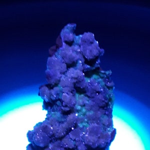 May include: A cluster of green and purple crystals on a metal stand under a blue light. The crystals have a rough, textured surface.