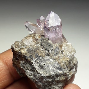 May include: A cluster of amethyst crystals with a purple hue, set in a rough gray rock matrix.