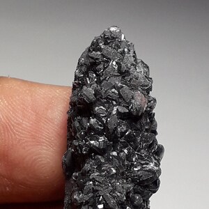 May include: A black, crystal-like mineral specimen with a rough, textured surface. The mineral is shaped like a pointed, elongated cone.