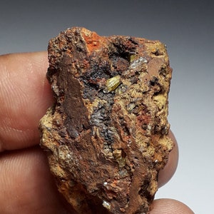 May include: A small, rough, brown rock with a few small, bright yellow crystals embedded in it.