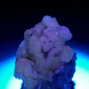 May include: A cluster of white crystals with a blue glow, set against a blue background. The crystals are clustered together in a rough, organic shape.