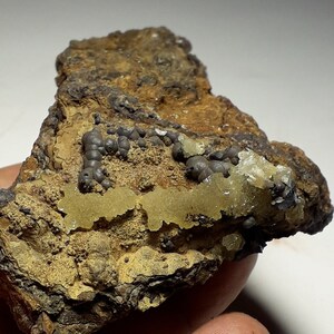 May include: A rough, brown rock with small, yellow and grey crystals. The crystals are clustered together in a random pattern. The rock has a natural, earthy look.