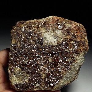 May include: A close-up of a rock with a large number of small, brown, sparkling crystals embedded in it.