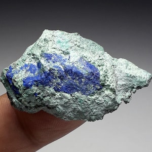 May include: A rough, green and blue mineral specimen with a blue azurite crystal formation. The specimen is about the size of a fingertip.