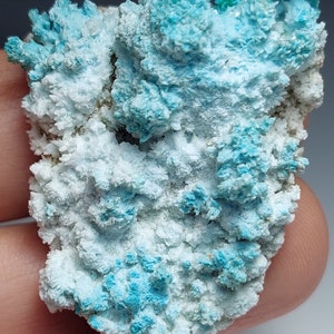 May include: A cluster of blue and white crystals. The crystals are arranged in a random pattern and have a rough, textured surface.