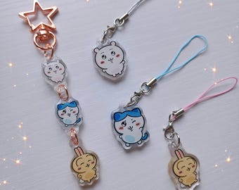 May include: Four different phone charms with cute cartoon characters. The charms are made of clear plastic with a white, blue, or yellow character design. Each charm is attached to a string.