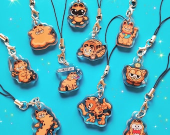 May include: A set of ten Garfield phone charms featuring different poses and expressions of the iconic orange cat. The charms are made of clear acrylic and have black string.
