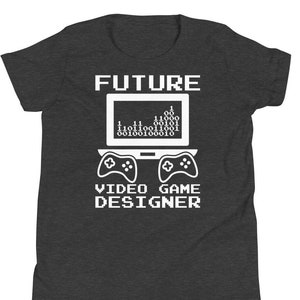 May include: Dark grey t-shirt featuring a white graphic. The graphic shows the word "FUTURE" above a laptop screen with binary code. Below the laptop are two game controllers, and the text "VIDEO GAME DESIGNER".