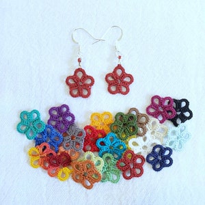 Puede incluir: Un par de pendientes rojos con forma de flor con ganchos plateados, exhibidos con una colección de piezas de ganchillo coloridas con forma de flor en varios colores. Los pendientes y las piezas de ganchillo están sobre una superficie blanca.