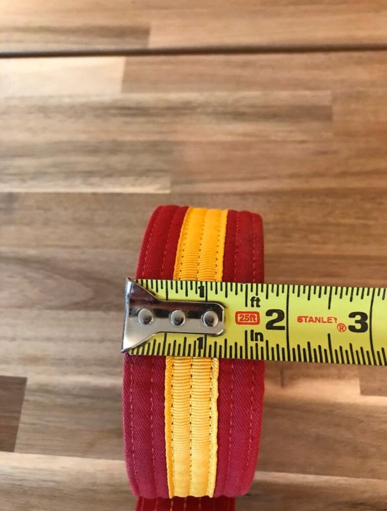 Puede incluir: Una cinta de tela a rayas rojas y amarillas medida con una cinta m&eacute;trica amarilla que dice "25ft" y "Stanley". La cinta tiene 2 pulgadas de ancho.