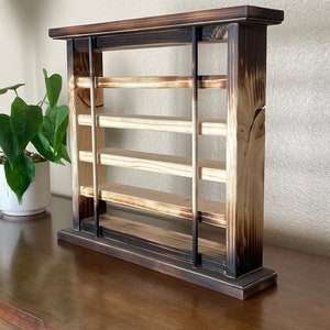 May include: A wooden shelf unit with a burnt finish. The shelf has four shelves and is supported by two vertical posts. The shelf is made of wood and has a rustic look.