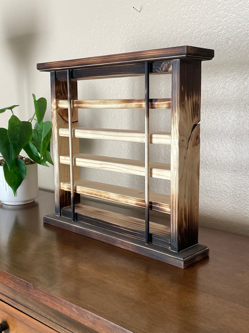 May include: A wooden shelf unit with a burnt finish. The shelf has four shelves and is supported by two vertical posts. The shelf is made of wood and has a rustic look.