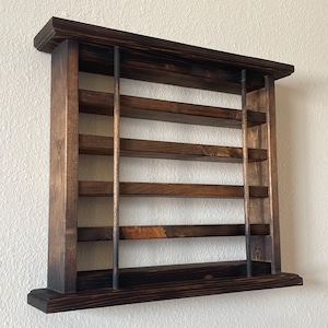 May include: A dark brown wooden wall shelf with five shelves and metal rods. The shelf is mounted on a white wall.