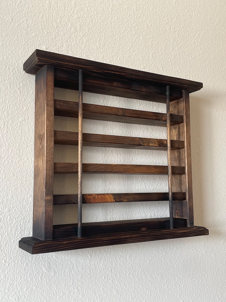 May include: A dark brown wooden wall shelf with five shelves and metal rods. The shelf is mounted on a white wall.