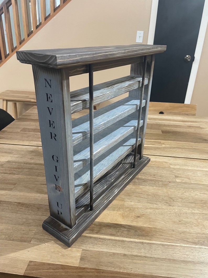 May include: A wooden shelf unit with five shelves, stained in a dark brown color with a gray wash. The shelf unit has a sign on the side that reads "NEVER GIVE UP".