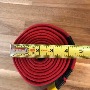 Puede incluir: Un cintur&oacute;n de tela rojo enrollado y medido con una cinta m&eacute;trica amarilla. La cinta m&eacute;trica indica 2, 3, 4 y 5 pulgadas. El cintur&oacute;n tiene 3 pulgadas de ancho.