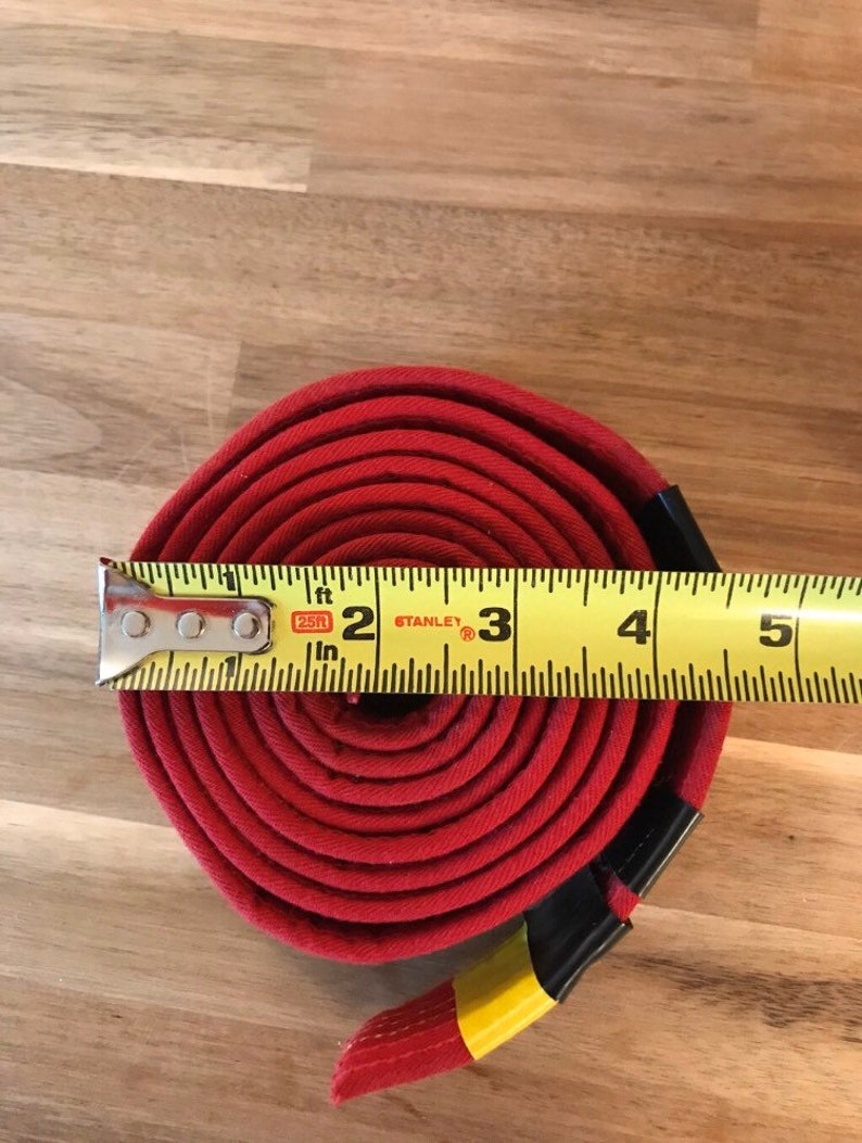 Puede incluir: Un cintur&oacute;n de tela rojo enrollado y medido con una cinta m&eacute;trica amarilla. La cinta m&eacute;trica indica 2, 3, 4 y 5 pulgadas. El cintur&oacute;n tiene 3 pulgadas de ancho.