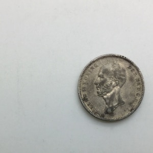May include: Silver coin featuring a portrait of a bearded man with the inscription "KONING DER NEDERLANDEN" around the edge.