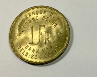 Könnte beinhalten: Eine goldfarbene Münze mit dem Text "BANQUE DU CONGO BELGE 1 FR BANK VAN BELGISCH CONGO" am Rand.