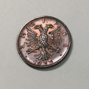 Peut inclure: Une pièce de monnaie de couleur cuivre avec un motif d'aigle à deux têtes et le texte "SHQIPN I" et "1935" autour de l'aigle.