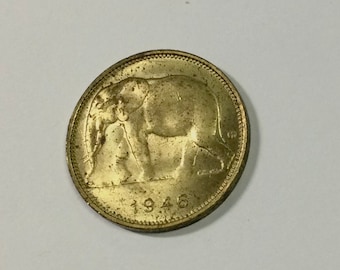 Könnte beinhalten: Eine goldfarbene Münze mit einem Elefantenmotiv und der Jahreszahl 1946 auf der Unterseite.