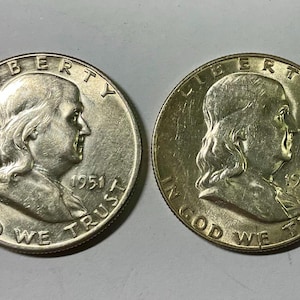 Könnte beinhalten: Zwei silberne Franklin-Halbdollar-Münzen. Die Münze links ist von 1951, die rechts von 1952. Beide zeigen ein Profil von Benjamin Franklin und die Worte "LIBERTY" und "IN GOD WE TRUST".