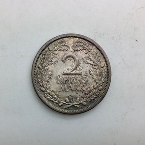 Könnte beinhalten: Eine silberne Zwei-Reichsmark-Münze mit einem Eichenblattmuster und dem Text "2 Reichsmark" in der Mitte.