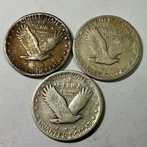 Könnte beinhalten: Drei amerikanische Vierteldollar-Münzen aus der Zeit. Jede Münze zeigt einen Adler mit ausgebreiteten Flügeln, die Worte "United States of America" und "Quarter Dollar". Die Münzen sind silberfarben und weisen Gebrauchsspuren auf.