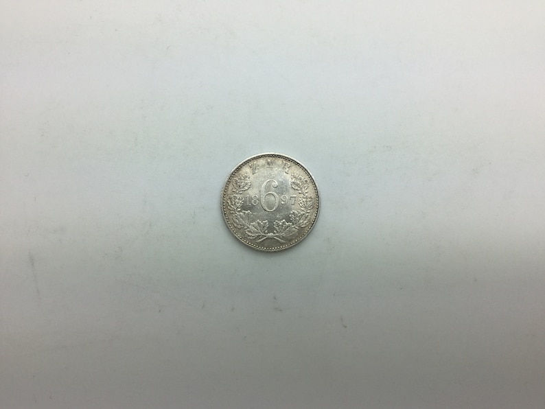Puede incluir: Una moneda de plata con el n&uacute;mero "6" y el a&ntilde;o "1897" inscritos en ella.