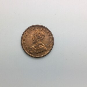 May include: A copper-colored coin with the inscription "GEORGE V KING EMPEROR" around the edge and a profile of a man wearing a crown.