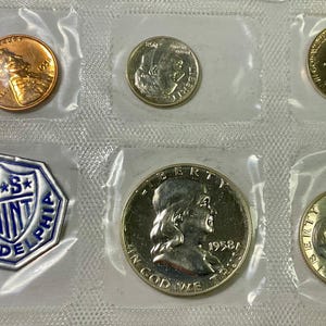 Könnte beinhalten: Eine Sammlung von alten US-Münzen, versiegelt in klarem Kunststoff. Das Set enthält einen Kupfer-Penny, einen Silber-Dime, einen Vierteldollar, einen halben Dollar und eine Münze mit dem Text "IN GOD WE TRUST" und "1958". Ein blau-weißes "U.S. MINT PHILADELPHIA" Emblem ist ebenfalls enthalten.