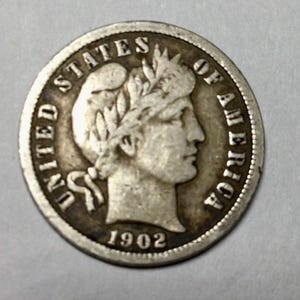 May include: A silver United States Liberty Head nickel coin with the year 1902 inscribed on the bottom.