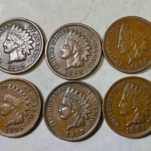 Peut inclure: Six pièces de monnaie anciennes Indian Head, chacune avec un profil d'Amérindien coiffé d'une coiffe de plumes. Les pièces datent de 1890, 1893, 1894, 1895, 1897 et 1901. Les pièces sont de couleur cuivre et présentent des signes d'usure.
