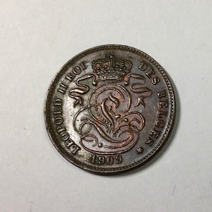 May include: A copper-colored Belgian coin with the inscription "LEOPOLD II ROI DES BELGES" and the year "1909" around a stylized crown and monogram.