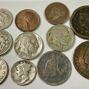 May include: A collection of antique coins, including silver and copper examples. The coins feature various designs, including portraits, shields, and dates. The coins are arranged on a white surface, showcasing their details and historical significance.