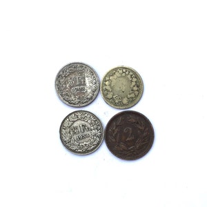 May include: Four silver and bronze Swiss coins. The coins feature a variety of designs, including a wreath, a flower, and the number "2".