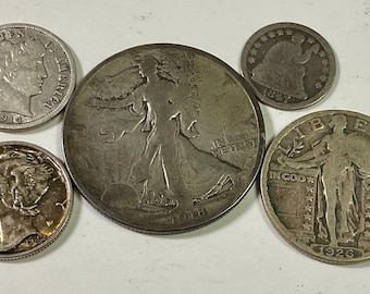 Op de afbeelding: Een verzameling antieke zilveren munten, waaronder een 1914 dime, een 1918 Walking Liberty half dollar, een 1926 Standing Liberty quarter en een Mercury dime. De munten zijn gerangschikt op een licht oppervlak.