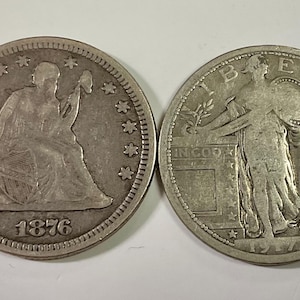 May include: Two silver coins. One coin shows a seated figure with the date 1876. The other coin features a standing figure with the inscription "LIBERTY" and the date 1917. Both coins have detailed designs and star patterns.
