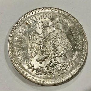 May include: A silver coin featuring the Mexican coat of arms: an eagle with a snake in its beak, perched on a cactus. The coin is inscribed with the words "ESTADOS UNIDOS MEXICANOS" and the year "1972".