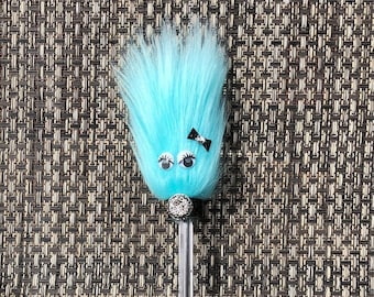 Op de afbeelding: Een blauwe, pluche pen met oogjes, een zwart strikje en een glinsterende strass neus.