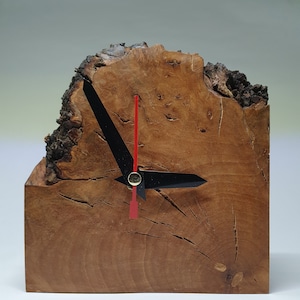 May include: A wooden clock with a red hour hand and a black minute hand. The clock is made from a natural wood slice with a rough bark texture.