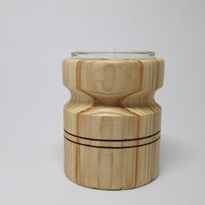 Könnte beinhalten: Ein Kerzenhalter aus Holz mit geometrischem Design. Der Halter ist aus hellem Holz mit natürlicher Oberfläche. Er hat einen klaren Glaseinsatz für ein Teelicht.