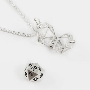 Può includere: Una collana d'argento con un ciondolo a forma di gabbia che si apre per rivelare un dado a venti facce d'argento.