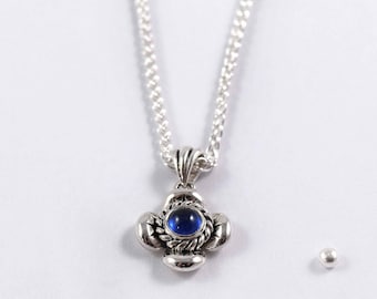 Puede incluir: Un collar de plata con un colgante de piedra azul. El colgante es un trébol de cuatro hojas con una pequeña piedra azul en el centro.